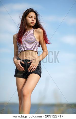 An attractive beautiful girl with long hair walking on a riverbank on a natural blurred background. Rest, summer, weekend, vacation concept.