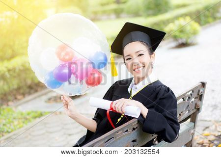 Portrait of happy young female graduates in academic dress and square academic cap holding word quotes of CONGRATS GRAD on balloon after convocation ceremony.