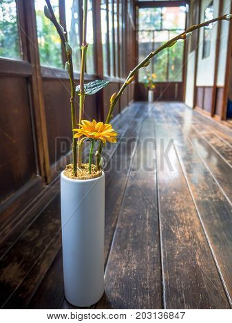 Close up of a flower vase with a yellow flower at indoor view of hall with a wooden floor, in Kyoto, Japan.