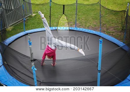 Slim woman tumbles on trampoline outdoor at summer day, top view