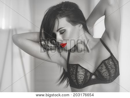 Sexy brunette woman in bra posing with closed eyes sensuality passions and desire. Selective coloring black and white with red lips