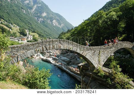 Tourists Visiting The Famous Roman Bridge Of Lavertezzo On Verzasca Valley
