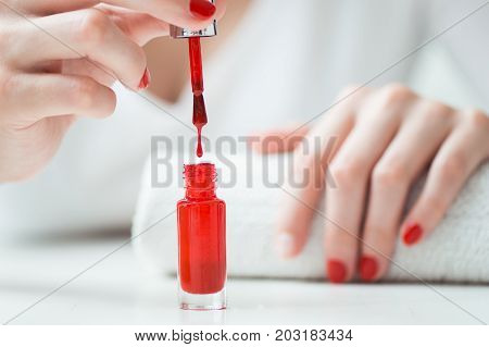 Close-up of red nail polish drop wih woman nails on backbround