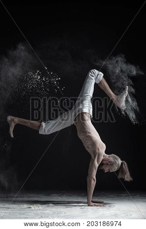 Flexible yoga man doing hand balance asana vrischikasana. Dust flying in air.
