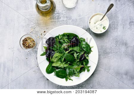 Spring salad with green leaves of spinach arugul on light stone background. Healthy food top view