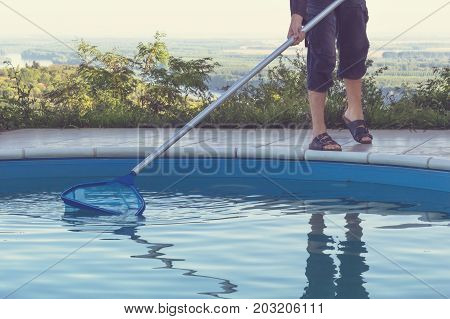 Man cleaning swimming pool of fall leaves with cleaning net in the morning.