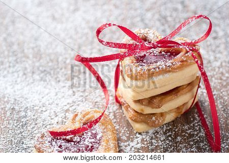 Fresh jam filled heart cookies with icing sugar and ribbon on a rustic wodden table. Ise it for a recipe or greeting card