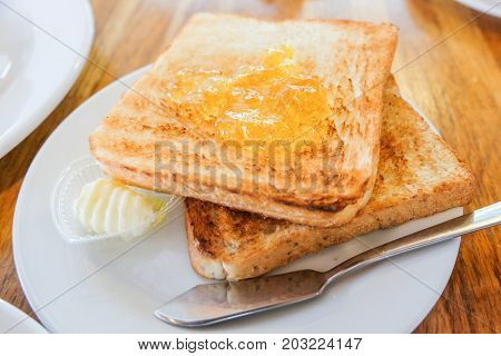Bread toast with orange jam cream and the knife steel serve on white dish for food background.