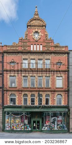 Dublin Ireland - August 7 2017: Red brick facade of historic Hodges & Figgis book store in Dawson Street under blue sky. Large windows display books and posters. Green trim around windows and door.