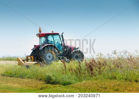 Aiguillon-sur-Mer France France - July 06 2016 : red tractor equipped with a large mower cuts the grass in a meadow