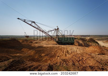 An industrial moving machine in the foundation pit. Yellow mobile crane working in the sandy quarry. Industry equipment on a blue sky background. Technology, cargo, commerce, transport concept.