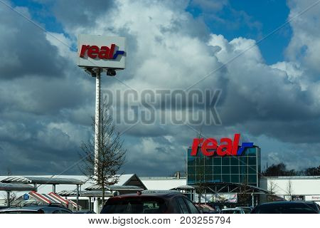 HEILIGENHAUS NRW GERMANY - FEBRUARY 24 2017: Real logo on department store in Heiligenhaus in front of a dramatic sky. Real Warehouse is a German trading chain.