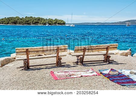 Wooden benches and towels on the beach Solta Croatia. Summer vacation. Sea with yachts scene.