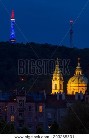 Church of Saint Nicholas lightup with lighting lookout tower Petrin behind at evening in Prague.