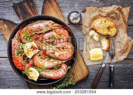 Traditional fried black tiger prawn with garlic bread as top view in a black frying pan 