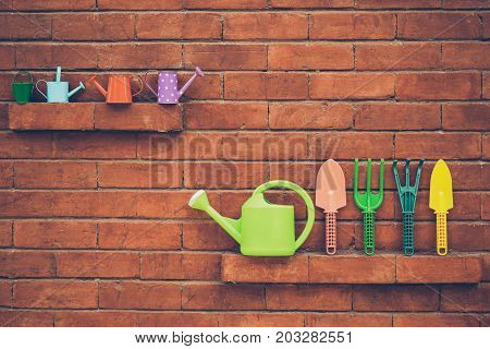 Colorful gardening tools on brick wall background - fork shovel rake bucket watering can