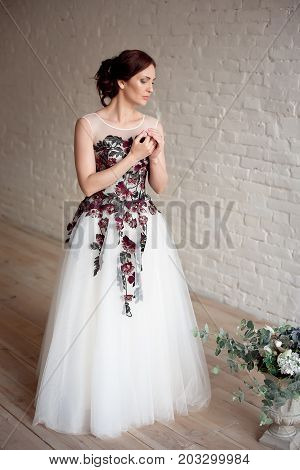 Full-length portrait of Beautiful luxurious female model with medium brown hair in a long fashinable dress standing in the room. Bridal clothes concept. Stylish wedding dress.