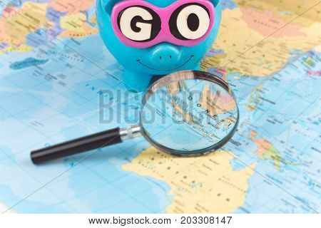 Going to Travel. Magnifier zoom spot on the map. Saving piggy bank with sunglasses and GO slogan staying on the world map.