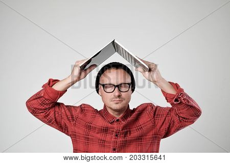 A young programmer in a black hat is holding opened laptopon his head. He s closes eyes trying to calm down. Concept of positive human emotion