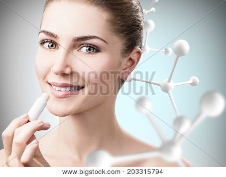 Beautiful young woman putting lipbalm in big molecules chain over gray background. Innovation cosmetics concept.