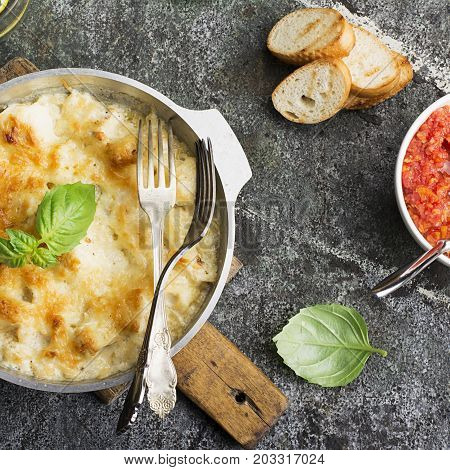Fragrant homemade casserole with cod and onion in cream sauce with horseradish under a cheese ruddy crust in a form on a gray background with crispy grilled toast. Top View