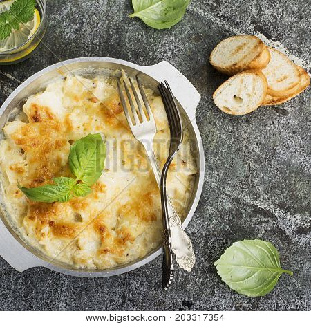Fragrant homemade casserole with cod and onion in cream sauce with horseradish under a cheese ruddy crust in a form on a gray background with crispy grilled toast. Top View