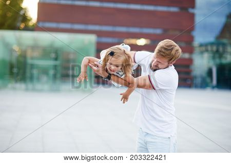Young dad is playing with a charming little daughter. The man holds the baby on handsand is turned together with her. The child laughs with pleasure.