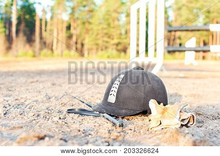 Equestrian equipment - helmet gloves and whip forgotten on the ground. Outdoors close-up.