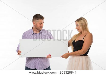 Young jocular couple portrait of a confident businessman showing presentation, pointing placard gray background. Ideal for banners, registration forms, presentation, landings, presenting concept.