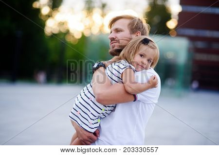 Young father holds the little daughter on hands. Man gently presses to himself the child. Baby put her head on her father's shoulder.