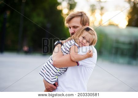 Young father holds the little daughter on hands. Man gently presses to himself the child. Baby put her head on her father's shoulder.