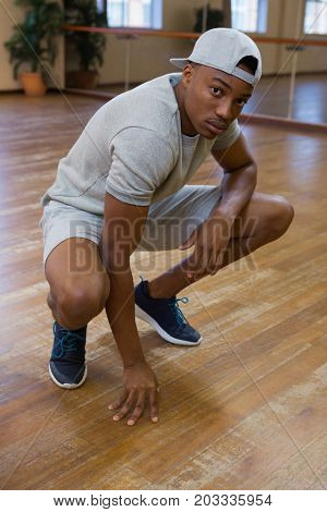 Full length portrait of male dancer crouching on hardwood floor in studio