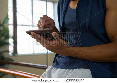 Mid section of male dancer using digital tablet by mirror in studio