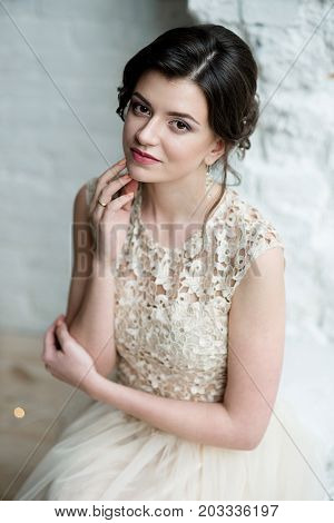 Half length portrait of brunette smiling woman dressed in sleeveless light evening dress.