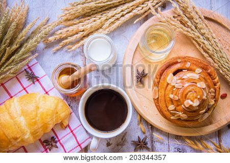 Fresh tasty bread with coffee and honey bee with milk on the table.
