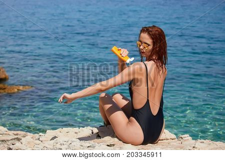 Girl in bikini applying sun lotion at seaside