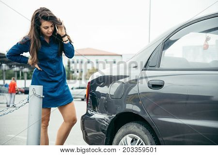 sad woman standing near car with scratch on parking and talking by the phone
