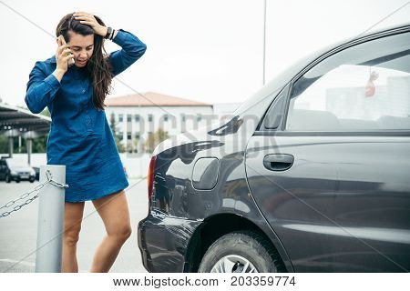 sad woman standing near car with scratch on parking and talking by the phone