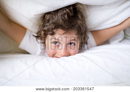 An Adorable little boy in white t-shit lying in bed