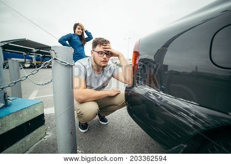 sad man looking on car scratch, woman stand behind him with sorrowful look