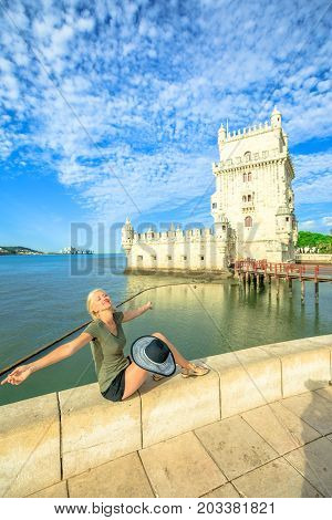 Happy woman with open arms at Belem Tower refleting. Torre de Belem is Unesco Heritage and symbol of Lisbon, in Belem District on Tagus River. Female tourist enjoys of most visited tourist attraction.
