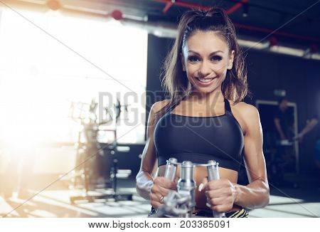Beautiful sexy athletic young brunette Caucasian girl working out training pumping up back lats muscles in the gym gaining weight on machines posing fitness and bodybuilding concept