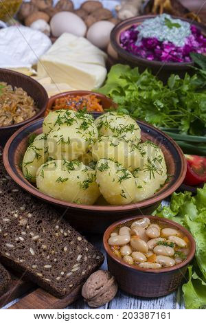Assorted food on wooden background. Boiled young potatoes beans braised cabbage beet salad with cottage cheese sliced cheeses pickled tomatoes korean carrot black bread with seeds green lettuce leaves spice. Bowls and plates with ukrainian food