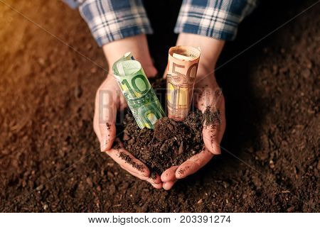 Hands with fertile soil and euro money banknotes female farmer handful of cultivated land that makes profit and steady income from sustainable agricultural activity like organic growth of crops