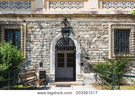 Facade of old stone house with opened door and bench at the entrance.
