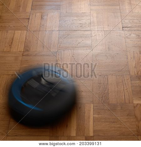 Robotic vacuum cleaner cleaning dust on laminate floor, natural movement, natural motion blur. image with square aspect ratio