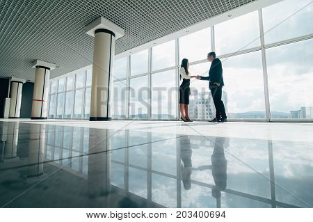 Businessman And Businesswoman Shaking Hands In Office With Big Panoramic Windows