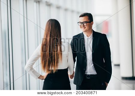 Businessman And Businesswoman Shaking Hands In Office With Big Panoramic Windows In Office Hall