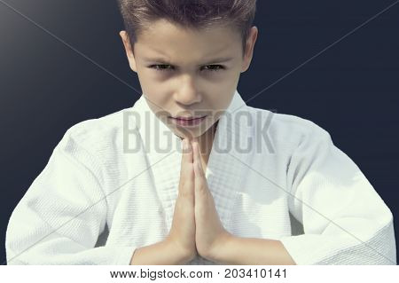 Portrait of a serious boy in a kimono greeting his opponent on a grey background