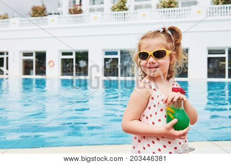 Cute little blonde at the pool and holding achild's cocktail .
